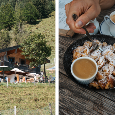 Seealm, Saalfelden, Hütte, Kaiserschmarrn, Links im Bild ist eine Berghütte auf einer Wiese zu sehen, umgeben von grünen Bäumen. Vor der Hütte befinden sich Sonnenschirme und eine Terrasse mit Gästen, die die Berglandschaft genießen. Rechts im Bild wird eine Hand gezeigt, die mit einer Gabel Kaiserschmarrn aus einer Pfanne isst, der mit Puderzucker bestäubt ist. Daneben steht ein kleines Schälchen mit Apfelmus sowie eine Tasse Kaffee auf einem Holztisch.