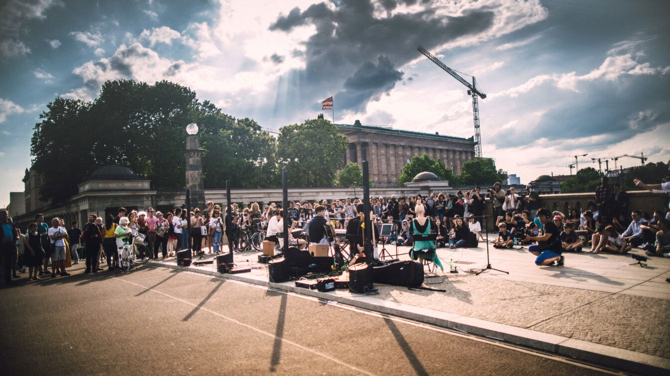 Fetê de la Musique Berlin (c)Jim Kroft Foto von einem Straßenkonzert, in der Mitte eine Band, herum stehen viele Personen