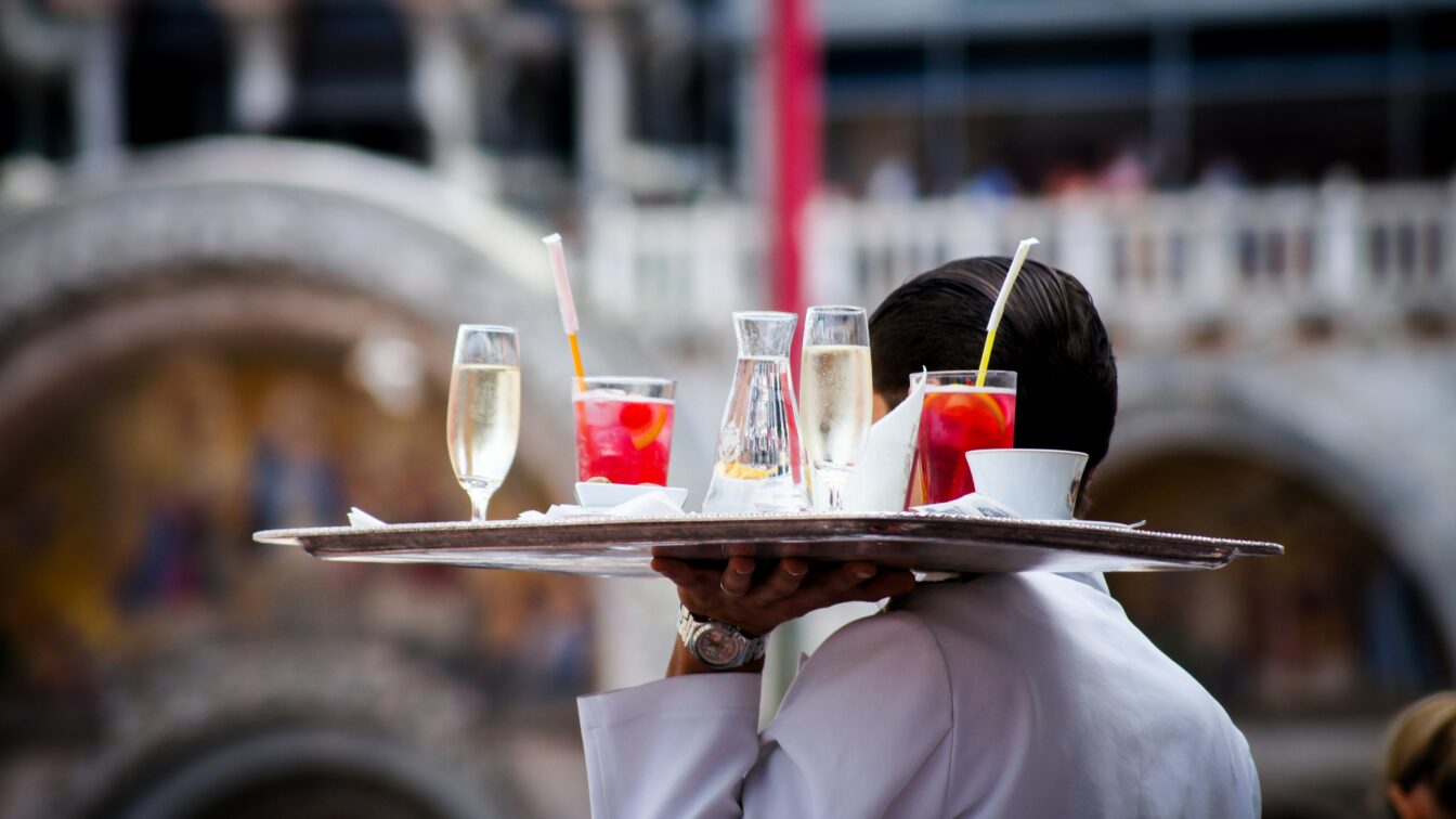 (c) Unsplash ein Kellner trägt ein mit Drinks beladenes Tablett